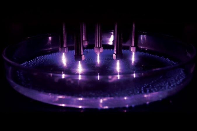 metal rods send an electric charge into a dish of water amid purple glowing light